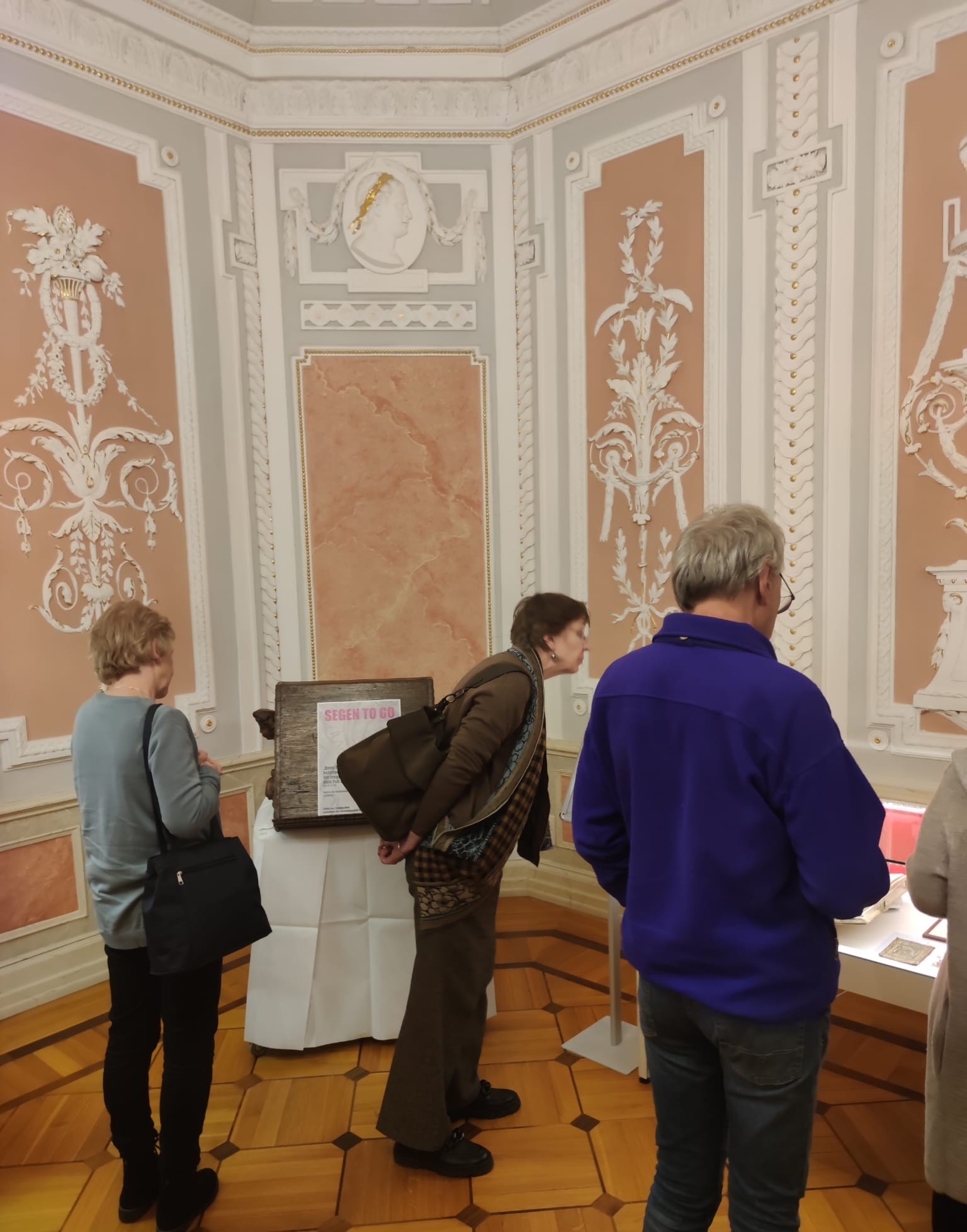 Ausstellung "Alle Wege führen nach Rom". Drei Personen schauen sich Ausstellungsstücke an. 